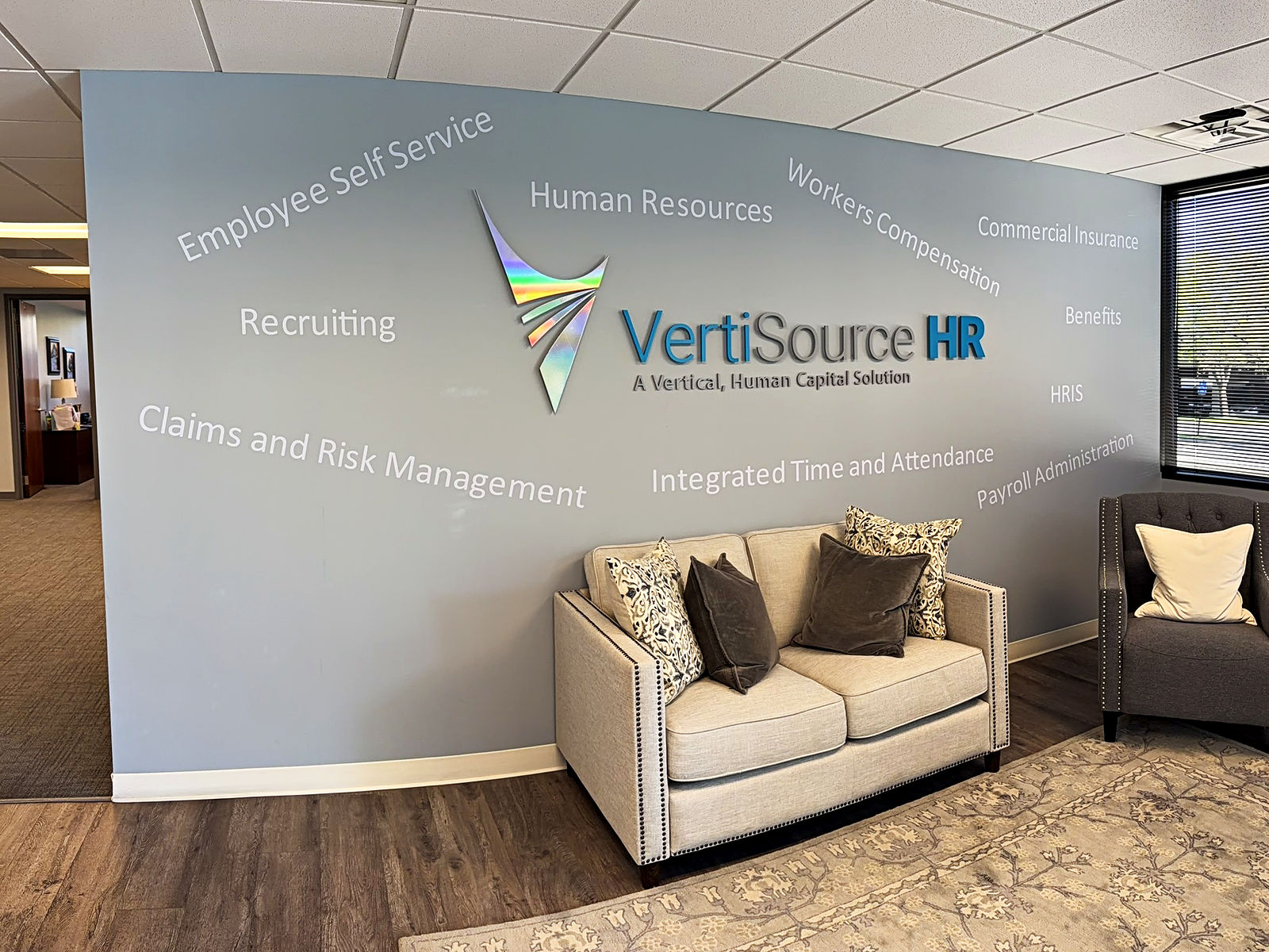 The logo wall in the lobby at VertiSource HR&rsquo;s Cottonwood Heights, Utah headquarters, with an office beyond the doorway