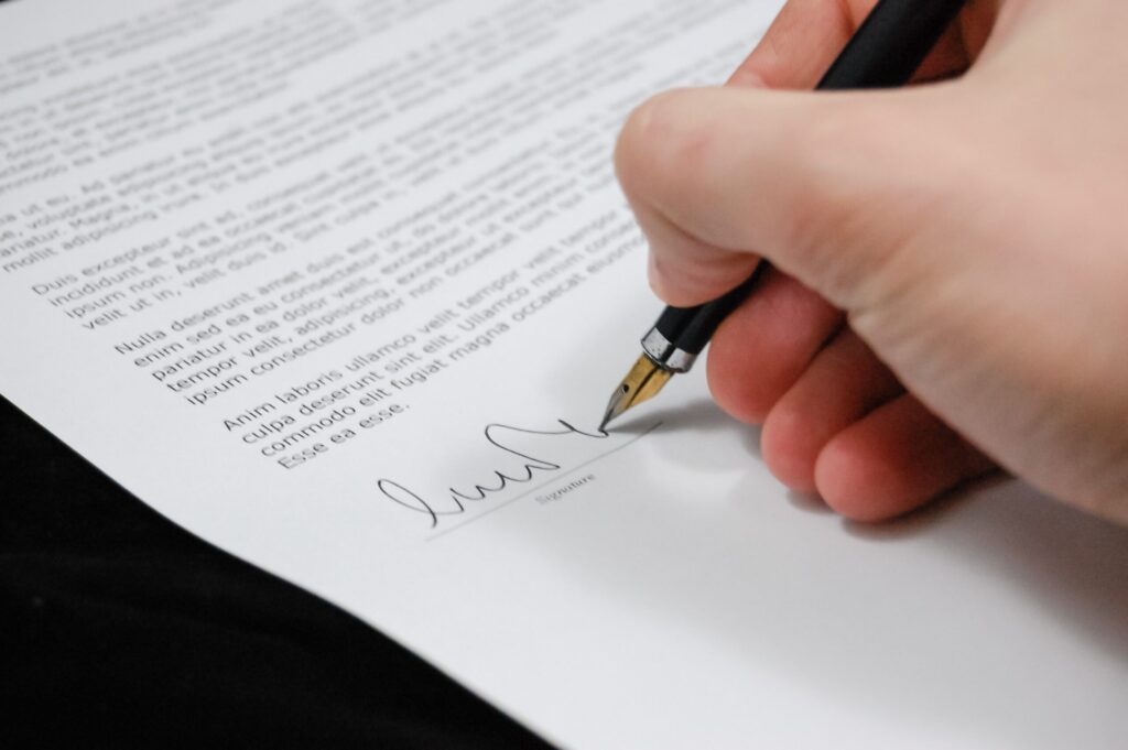a white hand signing a contract with a pen